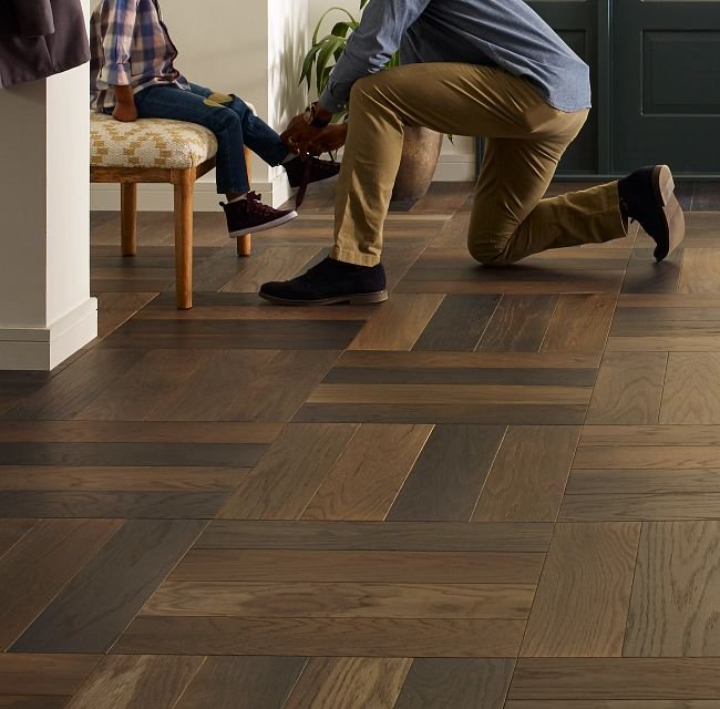 Man helping child wear shoes while kneeling on hard flooring - Wilmington Carpet